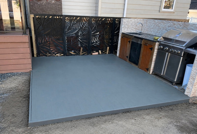 A large gray concrete deck slab installed in an outdoor backyard patio area next to a stainless steel grill, wooden cabinets, and a decorative black metal screen.