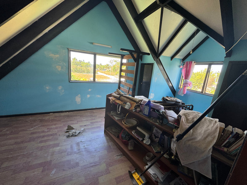 An attic room with blue walls, black exposed beams, wood flooring, and a cluttered wooden shelf and desk in the foreground.