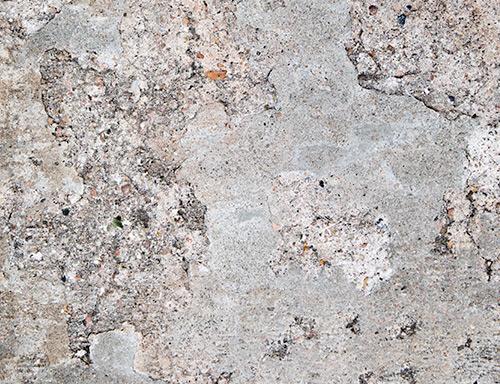 A close-up of a textured concrete surface with a mottled pattern of light gray, beige, and white tones, showing cracks, speckles, and weathered details.